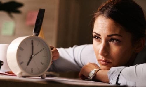 displeased-businesswoman-hitting-alarm-clock-with-hammer-office