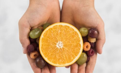 overhead-view-person-s-hand-holding-halved-orange-with-grapes-raspberry