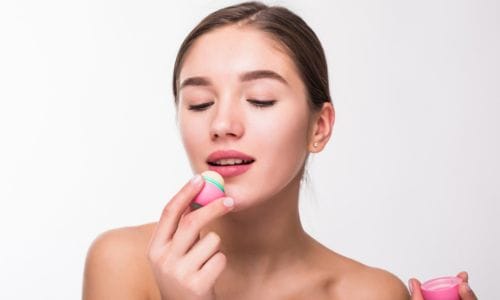 young-woman-applying-hygienic-lip-balm-white-wall